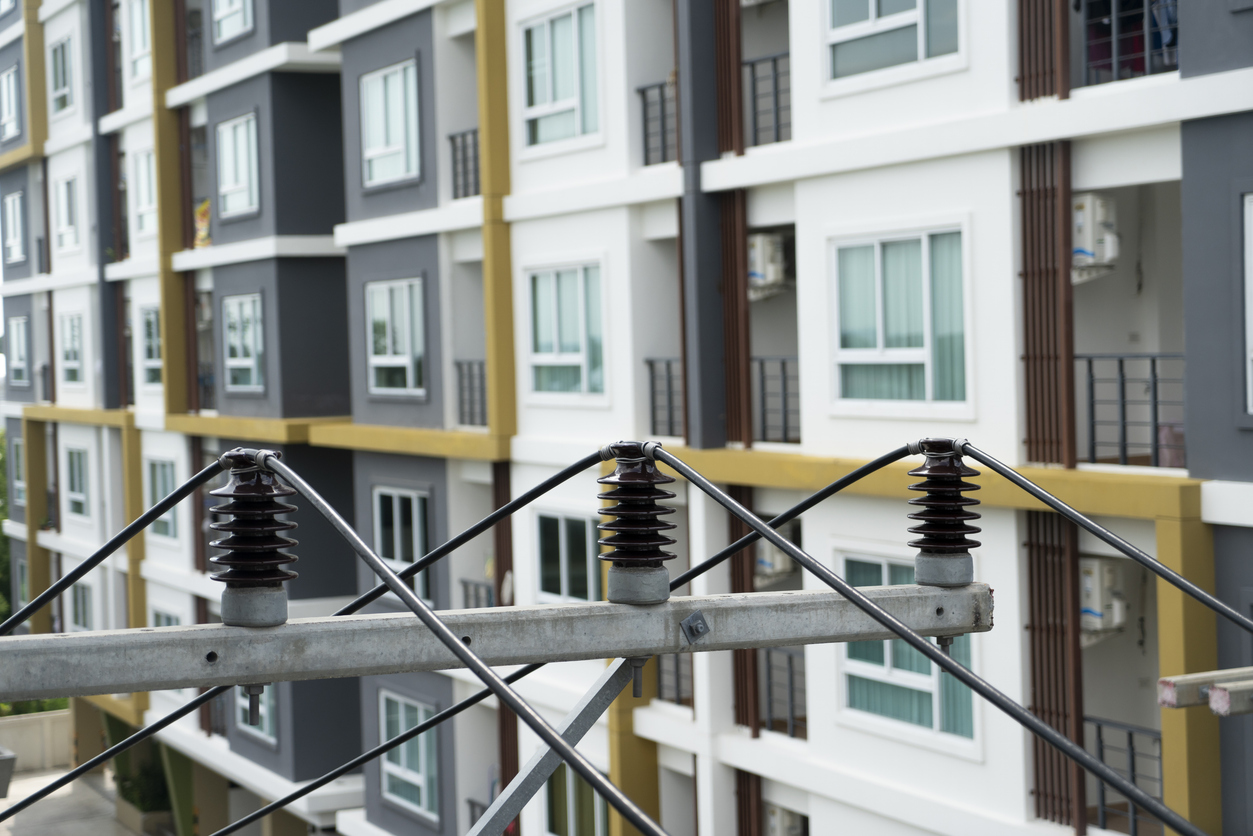 Apartment shopping, Apartment Mystery Shops, Apartment renters Journey Electrical wires with insulators stretch across the foreground, while a modern multifamily apartment building, showcasing numerous windows and advanced energy management systems, stands prominently in the background. Multifamily Journey Lens CX for the Apartment Industry